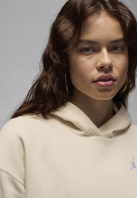 Felpa beige dalla vestibilità comoda, con tasca frontale e cappuccio con cordino. Un piccolo logo viola è visibile sull'area sinistra del petto.