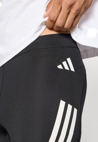 Svarta atletiska leggings med vita tre-randiga logodetaljer. Har ett slätt, stretchigt material och en figurnära design.