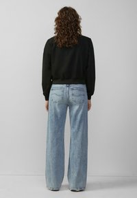 Zwarte sweatshirt met geribbelde manchetten en zoom, gecombineerd met lichtblauwe wijdere spijkerbroek met achterzakken en een vervaagde structuur.