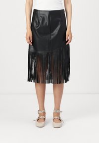 Fekete műbőr szoknya rojtos alsó széllel, testre simuló fazonnal és diszkrét varrási részletekkel. A modellen világos színű, pántos cipők vannak.