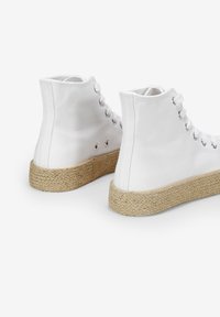 Zapatillas altas de lona blanca con suela de yute natural trenzado y ojales de metal para los cordones, con tacones redondeados y una textura suave.