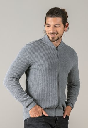 Grauer Reißverschluss-Pullover mit strukturiertem Strickmuster, geripptem Kragen und Bündchen. Mit schmaler Passform und seitlichen Taschen, getragen über dunkel gefärbten Hosen.