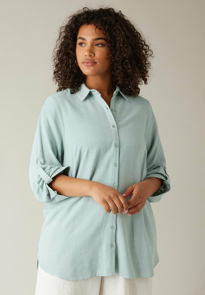 Hellblaues Button-Up-Shirt mit entspannter Passform, hochgerollten Ärmeln und weicher Textur. Verfügt über einen klassischen Kragen und eine durchgehende Knopfleiste.