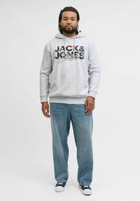 Grijze hoodie met kleurrijk "JACK & JONES" logo, ontspannen pasvorm, gedragen met lichtblauwe jeans en zwarte sneakers.