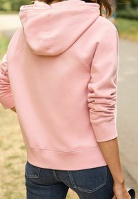 Felpa con cappuccio rosa caratterizzata da una texture morbida, con cappuccio arrotondato, maniche con polsini e un orlo che si trova appena sopra i fianchi.