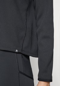 Black ribbed long-sleeve shirt featuring a tag at the hem, paired with fitted black leggings that have a side zipper pocket.