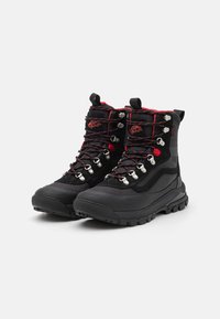 Black hiking boots with a textured surface, silver hardware, and red laces. High-top design featuring an accented heel and rugged sole.