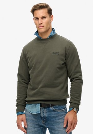 Olijfgroene sweatshirt met ronde hals en geribde manchetten, gelaagd over een lichtblauw denimshirt. Eenvoudig ontwerp met logo op de borst.
