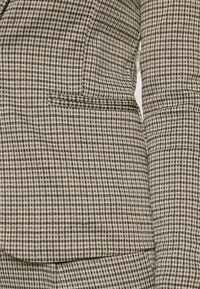 Geruite blazer met een mix van bruin, crème en zwarte patronen. Heeft een gestructureerd ontwerp, een notch revers en een enkele borstzak.