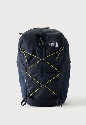 Sac à dos noir North Face Borealis Trail avec cordons élastiques jaunes et sangles frontales verticales, présenté sur un fond clair uni.