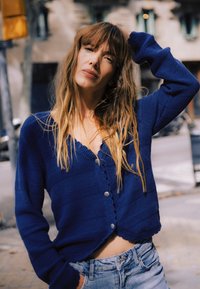 Marineblå strikket cardigan med strukturerede striber og fem knapper, båret over lyse denimshorts, afslappet pasform, ærmer i midterlængde.