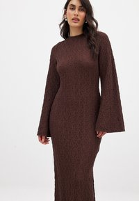 Robe longue marron texturée à manches longues avec une silhouette adaptée et des manches évasées, dotée d'un col haut et d'une finition en tissu lisse.