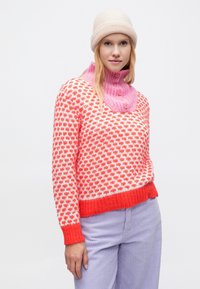 Červený a biely vzorovaný pletený sveter s ružovým rolákom a gombíkmi. V kombinácii so svetlofialovými manšestrovými nohavicami a béžovou čiapkou.