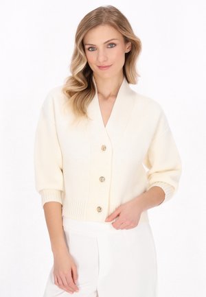 Cardigan crem cu decolteu în V, mâneci scurte, tiv ondulat și cinci nasturi aurii. Tricotul texturat oferă un aspect confortabil.