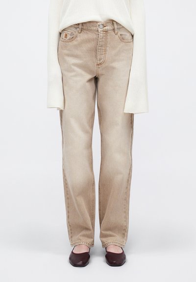 Beige denim jeans with a straight fit, high waist, and front pockets. Worn with a white ribbed sweater and dark flat shoes.
