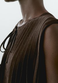 Brown knitted sleeveless top featuring ribbed texture, a scoop neckline, and a tie detail at the front. Simple, neutral design.