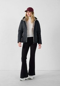 Zwarte pufferjack met een binnenvoering van luipaardprint, ritsluiting, gecombineerd met een witte geribde turtleneck, zwarte flared broek en een kastanjebruine pet. Zilveren sneakers.