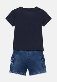 Μπλε ναυτικό βαμβακερό T-shirt με κοντά μανίκια, συνδυασμένο με σορτς σε στιλ τζιν που διαθέτει τσέπη και ξεθωριασμένο μπλε φόντο με διαβάθμιση. Ομαλή υφή.