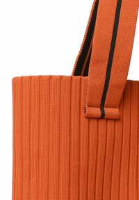 Borsa tote arancione a coste con superficie texturizzata e una tracolla a strisce nere. Il manico è fissato con un anello in tessuto coordinato.