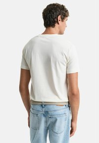 Hvit kortermet t-skjorte vist fra baksiden, med en jevn tekstur og rund hals, kombinert med lyseblå jeans og et vevd belte.