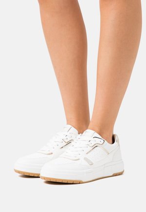 Scarpe atletiche bianche con tomaia in pelle testurizzata, lati perforati e accenti dorati, dotate di una suola imbottita e una suola piatta in gomma.