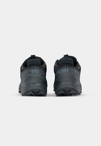Schwarze Trailrunning-Schuhe mit strukturiertem Obermaterial, robuster Ferse und tiefen Profilsohlen. Das "Salomon"-Logo ist auffällig platziert.