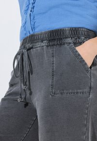 Šedé jogger kalhoty vyrobené z měkké tkaniny s elastickým pasem, stahovací šňůrkou a postranními kapsami.