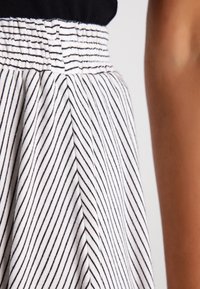 Gestreifter Stoffrock mit gerafftem Bund. Verfügt über abwechselnd weiße und marineblaue vertikale Streifen, die eine strukturierte Optik erzeugen.