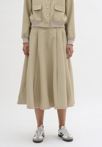 Beige two-piece outfit featuring a cropped bomber jacket with two pockets and a high-waisted, pleated skirt. Paired with white and black sneakers.