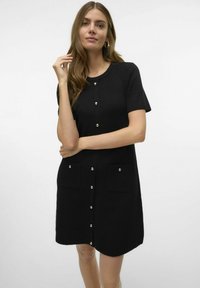 Vestido de punto negro con mangas cortas, con un escote redondo, cierre frontal con botones grandes y dos bolsillos de parche.
