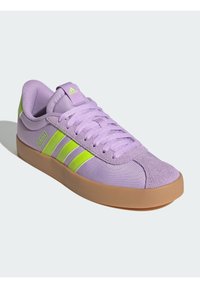 Jasnofioletowe trampki z trzema limonkowozielonymi paskami, miękka cholewka z tkaniny, teksturowany nosek i gumowa podeszwa w kolorze gumy.