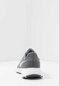Šedá sportovní obuv s texturovaným svrškem, polstrovanou bílou podrážkou a elegantním designem s výrazným bílým logem na straně.