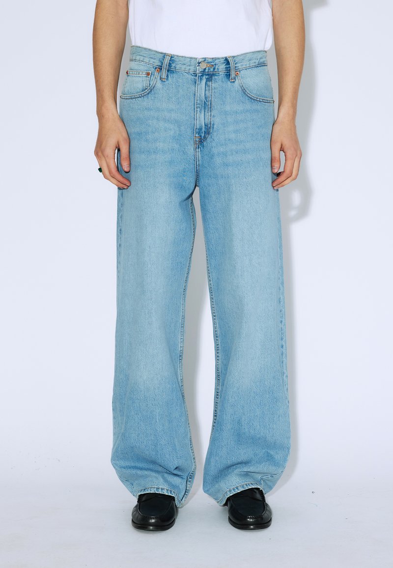 Jeans a gamba larga di colore blu chiaro realizzati in denim, con vita alta, cinque tasche e un leggero effetto sbiadito. Abbinati a scarpe nere.