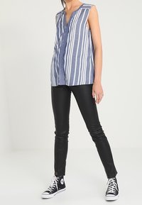 Top sin mangas a rayas azul y blancas, con un diseño de escote en V, combinado con pantalones ajustados de cuero negro y zapatillas altas negras.