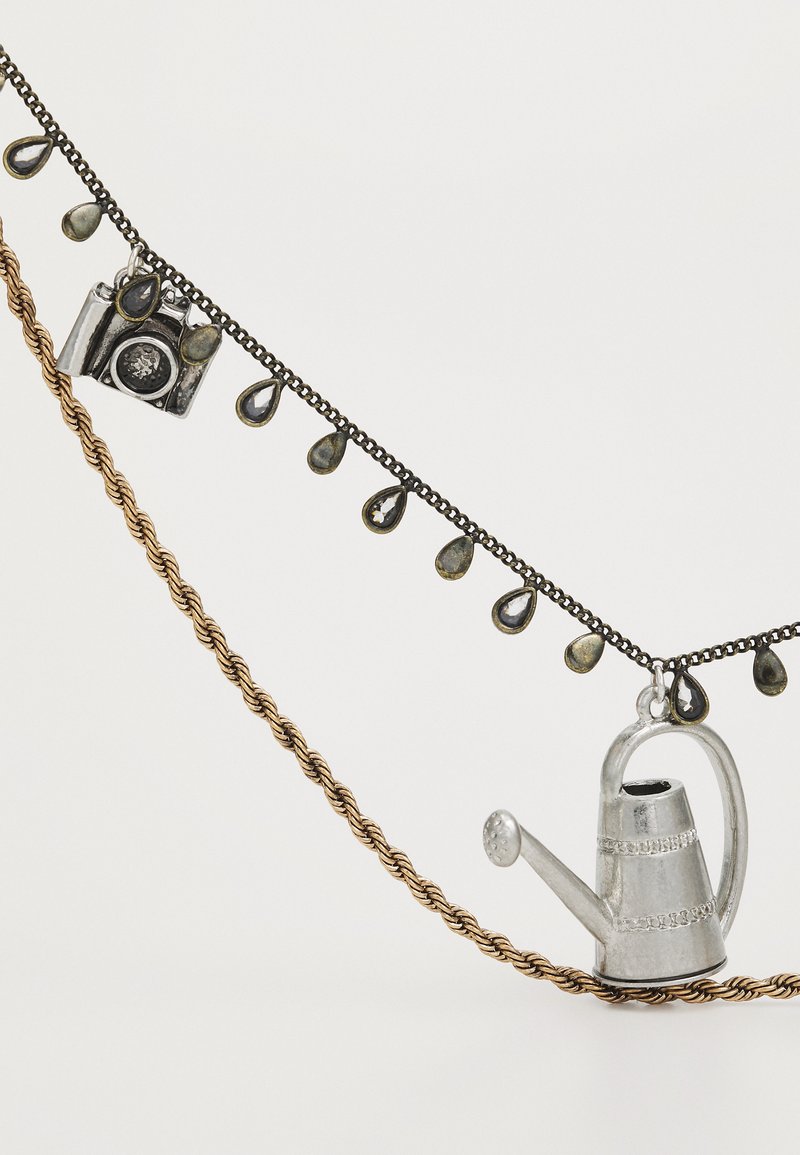 Collar de metal que presenta encantos de una regadera plateada y una cámara, adornado con acentos en forma de lágrima, sobre cadenas trenzadas de oro y negro.