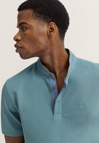 Poloshirt aus leichtem Baumwollstoff in Hellblau mit strukturiertem Finish, mit einem Kragen, zwei Knöpfen und kontrastierenden blauen Akzenten.