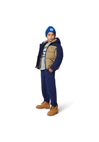 Gevoerde marineblauwe en tan jas met een capuchon, blauwe gebreide beanie, lichtblauw T-shirt met opdruk, marineblauwe broek en tan laarzen met gele veters.