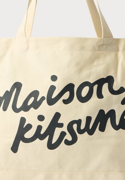 Plátěná taška v béžové barvě s černým textem "Maison Kitsuné", vybavená pevnými uchy a hladkým, netexturovaným povrchem.