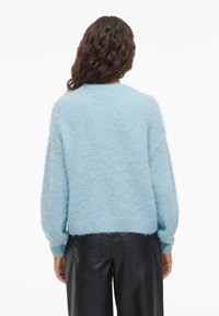 Svetlo modri puhasti pulover z ohlapno prileganjem, rebrastimi manšetami in robom. Mehka tekstura, rahlo prevelik dizajn, prikazan pogled od zadaj.