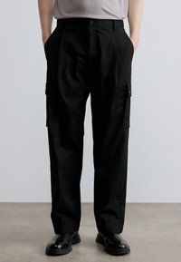 Mustad saapad sirgete säärtega, küljetaskutega ja siledapinnaline tekstuur. Valmistatud kerge, vastupidava kangaga.