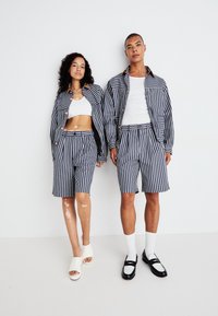Stripede stoffer i marineblått og hvitt; inkluderer en jakke og shorts. Kvinnen har på seg en hvit tank topp, mannen en hvit t-skjorte, og sko.