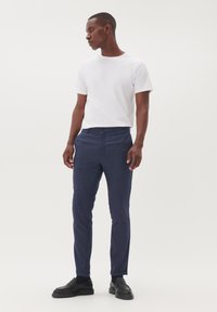 Camiseta blanca de manga corta combinada con pantalones oscuros de textura azul, con cierre de botones y puños enrollados, complementada con mocasines negros.