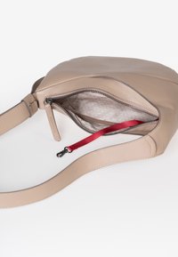 Beige leren crossbody tas met open rits, lichtpatroon stof interieur en een rode schouderband met zwarte clip aan de binnenkant.