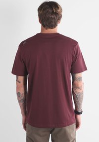 T-shirt en coton bordeaux à manches courtes et col rond léger. Présente un petit logo sur l'épaule et une texture lisse.