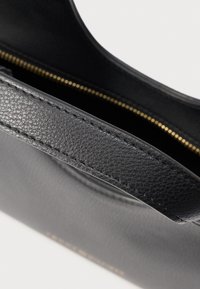 Čierna kožená taška s textúrovaným povrchom, vybavená horným úchytom a zlatým zipsom pozdĺž otvoru. Vnútro je viditeľné.