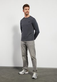 Sudadera gris con cuello redondo y mangas largas, combinada con jeans gris claro y zapatillas deportivas multicolores. Diseño sencillo y ajuste casual.