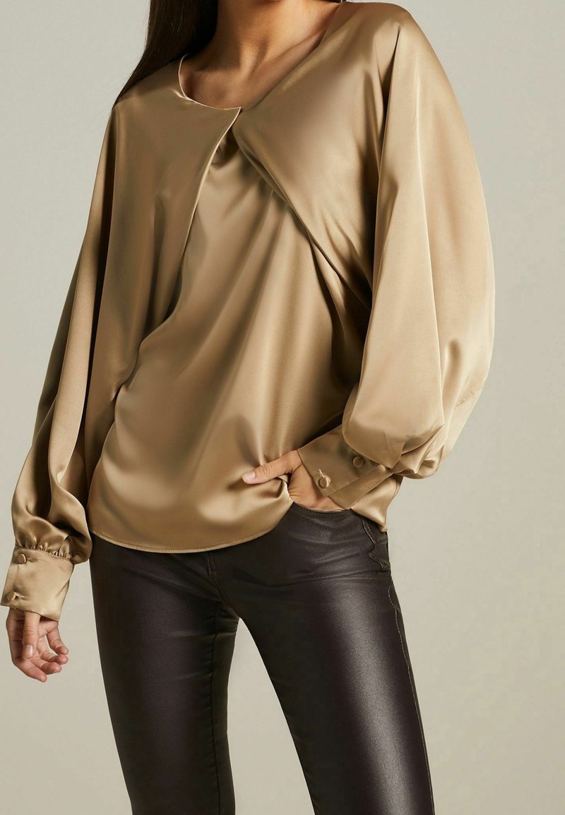 Bronze satin long-sleeve top with a wide neckline and front pleat detail. Features fitted cuff buttons and drapes softly over the body.