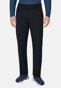 Schwarze Hosen mit geradem Bein, aus weichem Stoff, mit vorderen Taschen und einem Knopfverschluss, kombiniert mit blauen Sportschuhen.