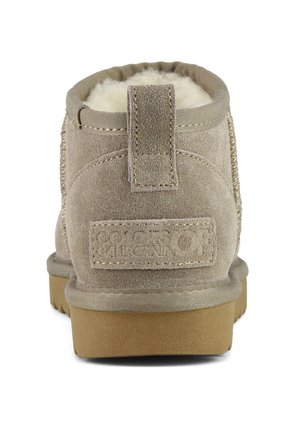 Bottine en suède beige avec une doublure en fourrure douce, une languette à l'arrière, des détails cousus et une semelle en caoutchouc tan avec un accent de logo.