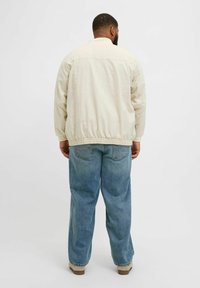Beige lightweight jacket with elastic cuffs and hem. Worn over faded blue wide-leg jeans. Plain design with no notable patterns or prints.